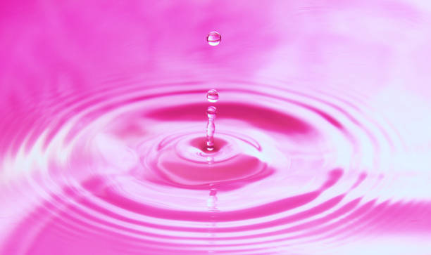 istock Drops of water fall into the water, forming perfect concentric circles. Abstract pink background 1249490520