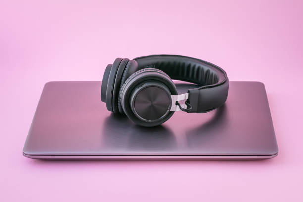Closed laptop and earphones. Metallic notebook and black portable headphones on a pink background. Entertainment concept of virtual reality. stock photo