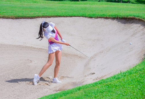 Thai young woman golf player in action swing in sand pit during practice before golf tournament at golf course