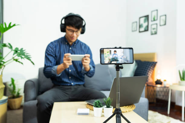 istock Asian man online influencer recording video live streaming, using digital smartphone camera present product review for theme about video blogging focus on camera screen show on social media 1249501948