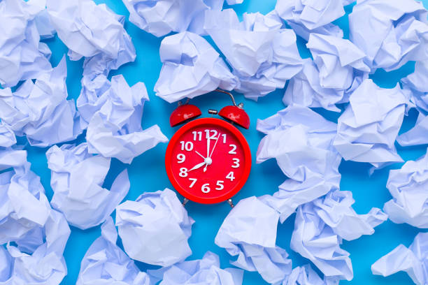 istock Red alarm clock with white crumpled paper balls on a blue background. 1249503396