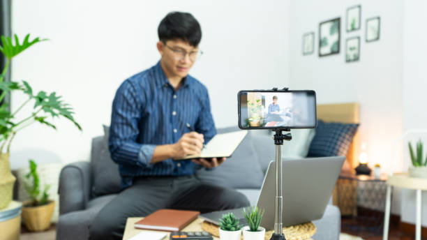 istock Asian man online influencer recording video live streaming, using digital smartphone camera present product review for theme about video blogging focus on camera screen show on social media 1249503409