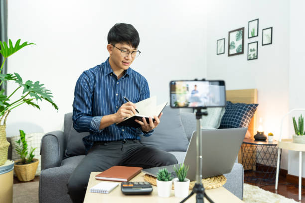 istock Asian man in headphones writing notes in notebook watching webinar video course studies via laptop at home lecture study online, E-learning concept 1249503579