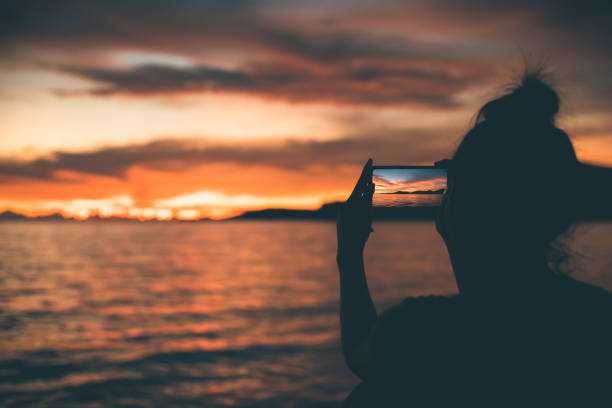 istock silhouette women use mobile phone for take a shoot seascape with sunset. 1249509088