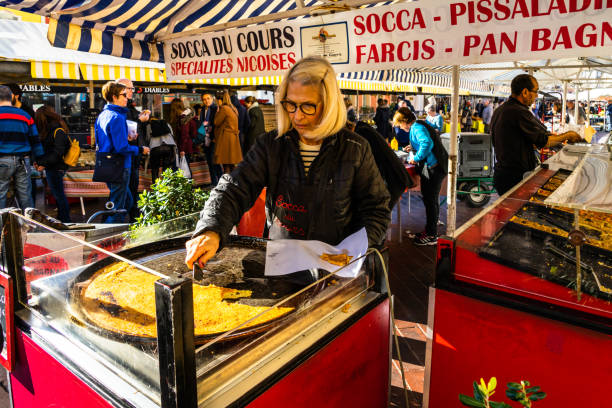 A woman slicing the “socca” at the market of Cours Saleya, Nice, France Nice, France, January 2020 – A woman slicing the “socca” at the market of Cours Saleya. Socca is a a sort of pancake made with chickpea flour and typical in Nice blini photos stock pictures, royalty-free photos & images