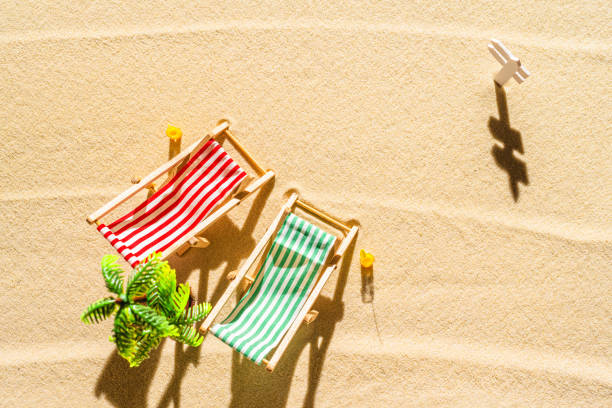 vue aérienne de deux chaises longues, transat, salon, verre de jus d’orange, palmier sur la plage de sable fin. concept d’été et de voyage. minimalisme - beach tropical climate palm tree deck chair photos et images de collection