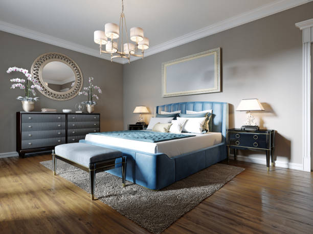 A modern bedroom in an eclectic style. With a double blue bed, black dressing table and chest of drawers with decor. beige walls and white wardrobe.