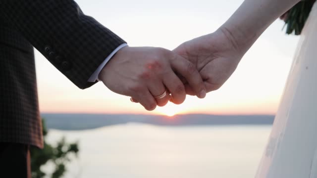 Wedding couple holds hands at sunset. The sun's rays shine through their fingers. Love, Happiness and Friendship. Hands close up at sunrise.
