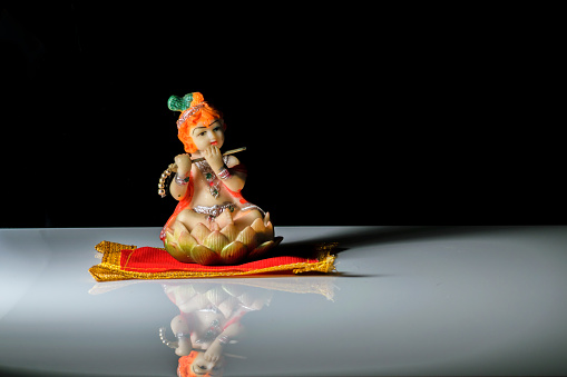 Una escultura aislada del dios indio Lord Krishna tocando la flauta sentado en una estera. Sobre una mesa blanca reflectante con un fondo oscuro photo