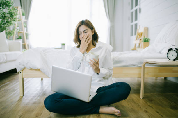 donna assonna stanca che sbadiglia, lavora a casa e tiene in mano una tazza di caffè, un lavoro troppo troppo e un concetto di privazione del sonno - yawning women drink coffee cup foto e immagini stock