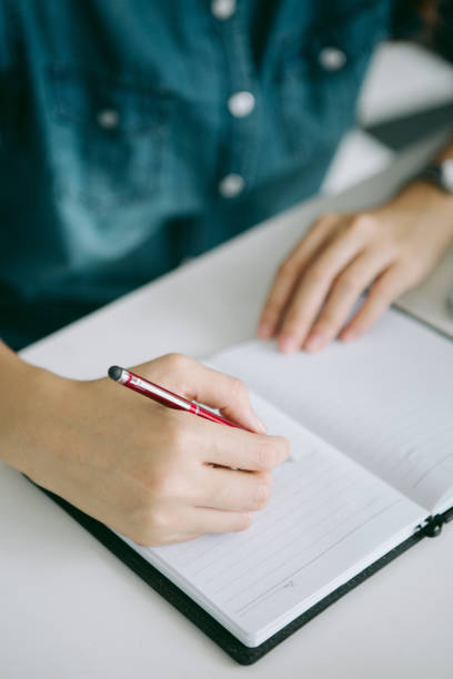 istock woman's hand with pen writing on book 1249528783