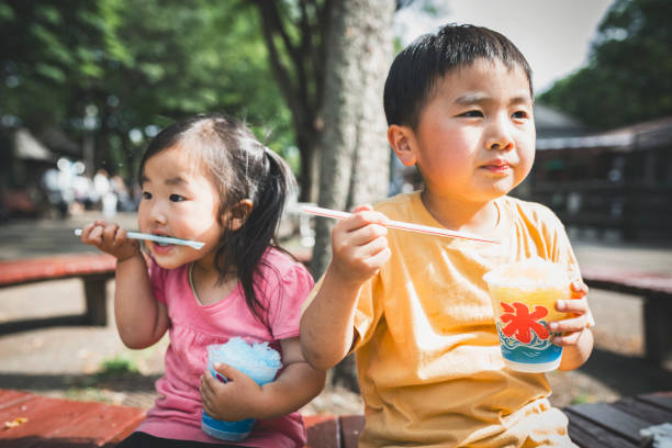 Asian brother and sister eating Japanese traditional shave ice on the bench together.