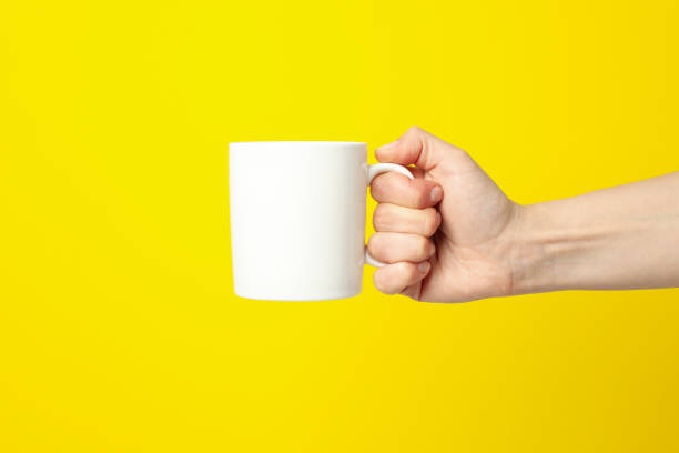 istock Female hand holding white cup on yellow background, space for text 1249552762