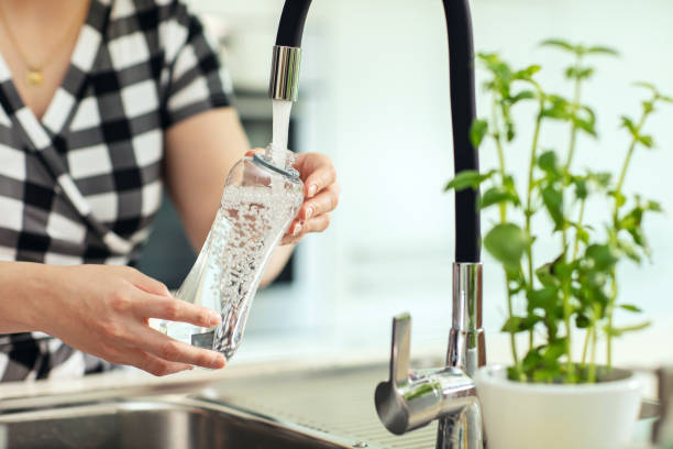 Pouring water into the bottle. Woman in background pours water from the sink to the reusable bottle stock photo