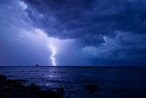 A storm front with rain and curved lightning striking the sea near an abandoned marine science platform