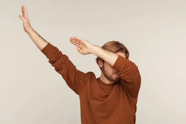 Photo of Dabbing movement. Portrait of optimistic carefree man wearing sweatshirt standing in dab dance pose