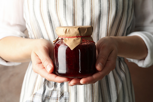 Woman holds glass jar with strawberry jam, close up