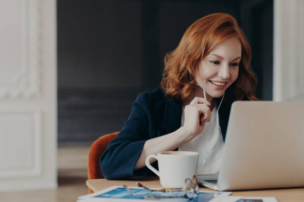 istock Happy smiling female entrepreneur has online conference via modern laptop computer, connected to wireless internet at home, uses earphones to hear interlocutor better, sits in coworking space 1249565559