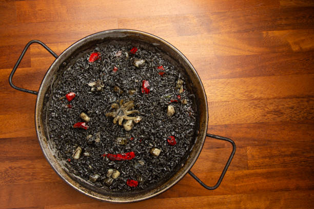 istock Black rice with squid in paella pan on wooden background 1249566719
