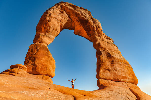 Young woman standing under Delicate Arch in Arches National Park, Utah, USA Young woman standing under Delicate Arch in Arches National Park, Utah, USA,Nikon D3x slickrock trail stock pictures, royalty-free photos & images