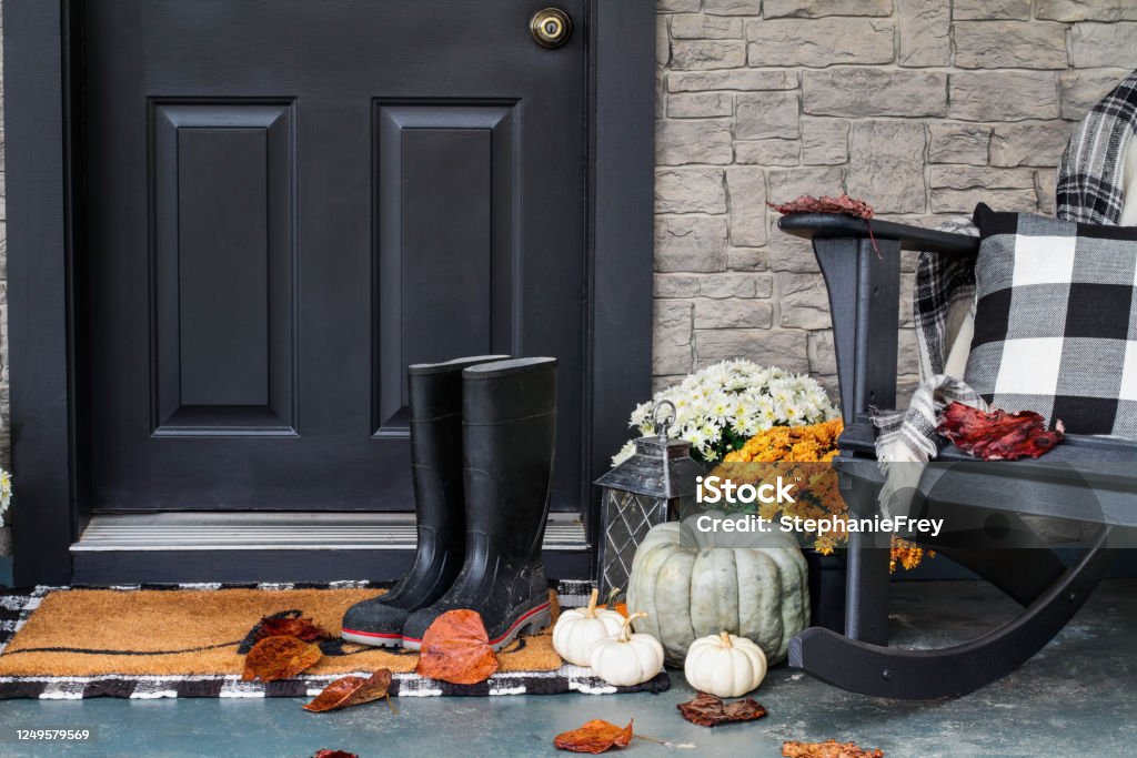 Front Porch Decorated for Autumn with Buffalo Plaid Traditional style front porch decorated for autumn with rain boots, heirloom gourds,  white pumpkins, mums and rocking chair with buffalo plaid pillow and throw blanket giving an inviting atmosphere. Autumn Stock Photo