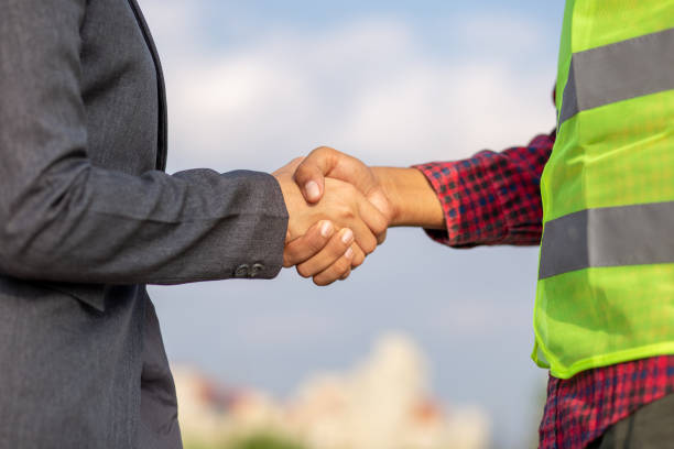 Businesswomen and foreman shake hands together. Engineer and manager teamwork and checking at site construction . stock photo