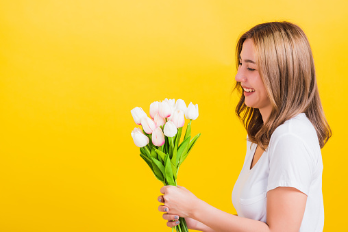 Portrait Asian Thai beautiful happy young woman smiling, screaming excited hold flowers tulips bouquet in hands and she looking to flowers, studio shot isolated on yellow background, with copy space
