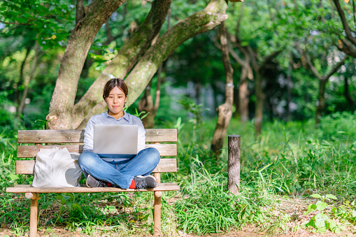 A young woman is using a laptop peacefully in a public park.