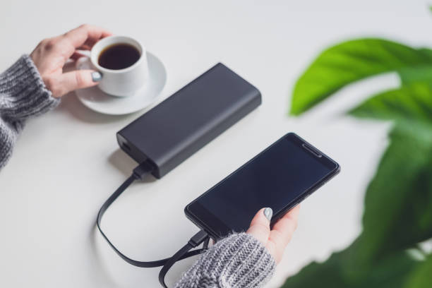 The phone is charged using a portable charger. The Power bank is connected to the phone via a cable. The girl charges her phone and drinks coffee The phone is charged using a portable charger. The Power bank is connected to the phone via a cable. The girl charges her phone and drinks coffee. usb port photos stock pictures, royalty-free photos & images