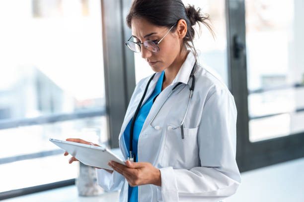 istock Beautiful female doctor using her digital tablet while standing in the consultation. 1249601200