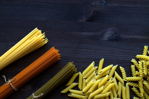 istock raw spaghetti and pasta on a wooden table with copy space. top view. uncooked wheat, Tomato and Spinach spaghetti and fusilli, penne on a dark background. Italian Cuisine 1249607034