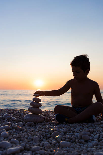 małe dziecko bawiące się kamieniami na plaży o zachodzie słońca - stone zen like buddhism balance zdjęcia i obrazy z banku zdjęć