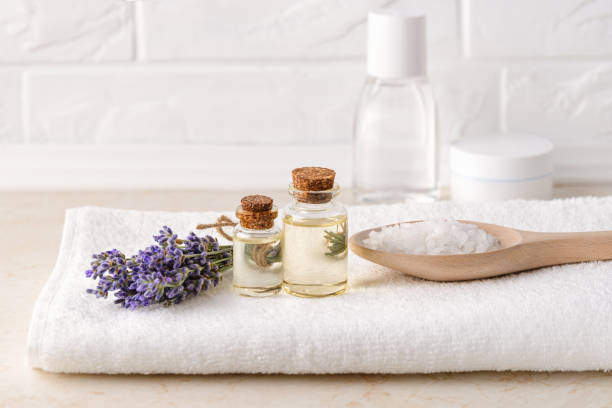 Fresh fragrant lavender, lavender essential oil and cosmetic bath salt on a white terry towel in a bathroom. Home made spa, skincare and cosmetology concept. Fresh fragrant lavender, lavender essential oil and cosmetic bath salt on a white terry towel in a bathroom. Home made spa, skincare and cosmetology concept. Front view. bath salt photos stock pictures, royalty-free photos & images