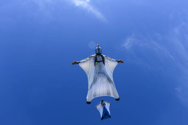 les aviateurs de costume d’aile glissent à travers le ciel bleu à l’unisson - wingsuit photos et images de collection