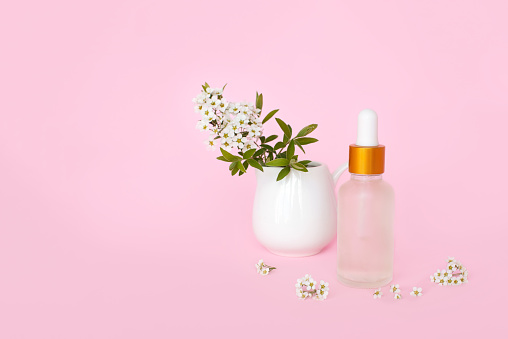 Glass cosmetic bottle with oil. Glass container for a cosmetic product for women with small white flowers on a pink background.