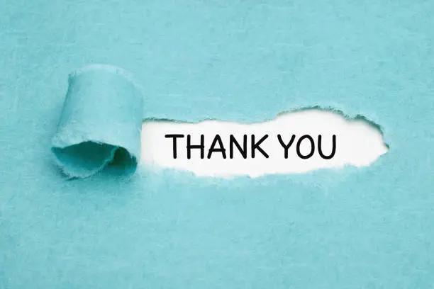 Handwritten text Thank You appearing behind ripped blue paper. Appreciation, gratefulness, or thankfulness concept.
