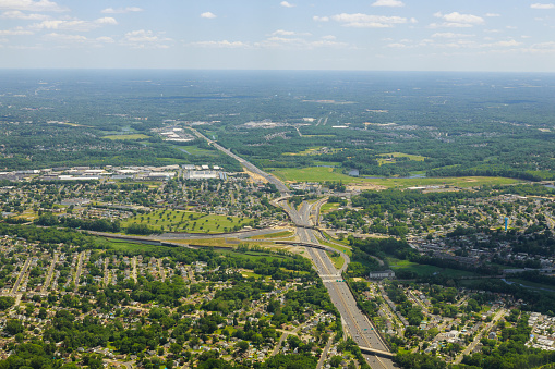 Aerial view of white clouds above a town village with rows of buildings and curvy streets between green fields in summer.