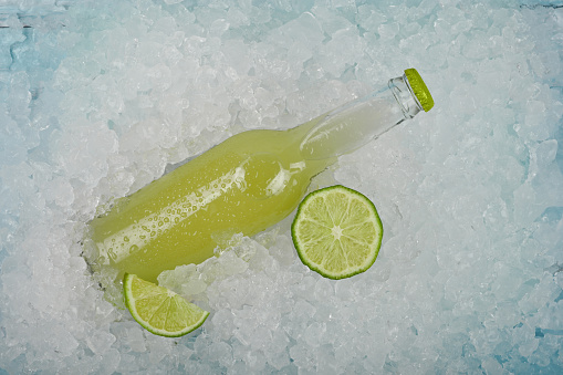 Close up one glass bottle of cold green juice cocktail with cut slice of lime on crushed ice at retail display, elevated high angle view