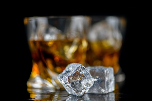 Glass of whiskey or other alcohol with cube ice on black background
