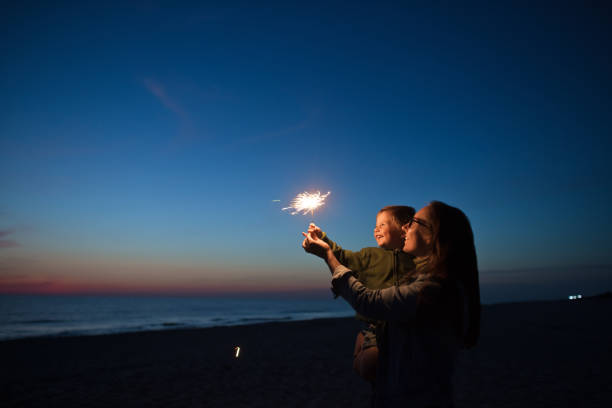 Family with sparklers on the beach in sunset Happy little boy looking at sparkler with his parent near the sea sparkler stock pictures, royalty-free photos & images