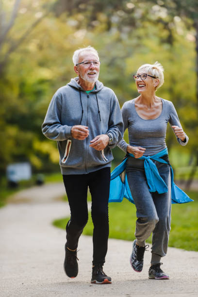 улыбаясь старший пара бег трусцой в парке - senior adult running jogging senior women стоковые фото и изображения