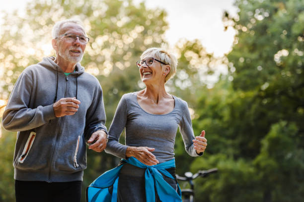 älteres paar im park joggen lächelnd - aktiver lebensstil stock-fotos und bilder