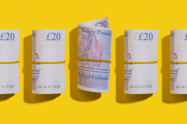 двадцать фунтов рулонов плоский лежал на желтом фоне - british currency pound symbol currency stack стоковые фото и изображения