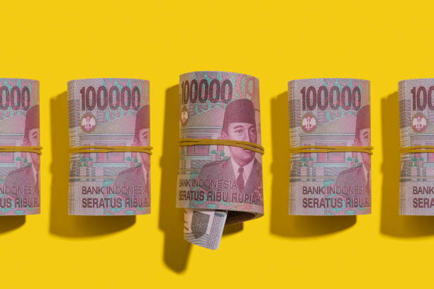 indonesische rupiah rollen flach auf gelbem hintergrund liegend - indonesian currency stock-fotos und bilder