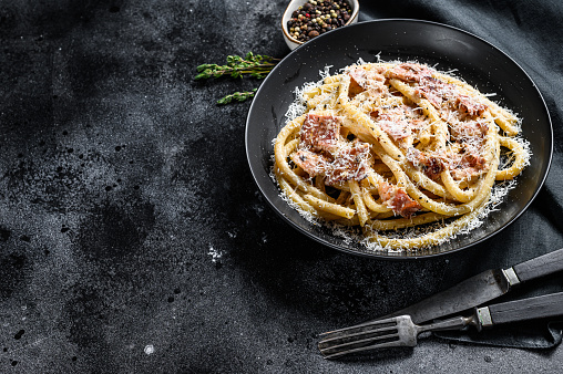 Pasta Carbonara on black plate with parmesan, bucatini. Black background. Top view. Copy space.
