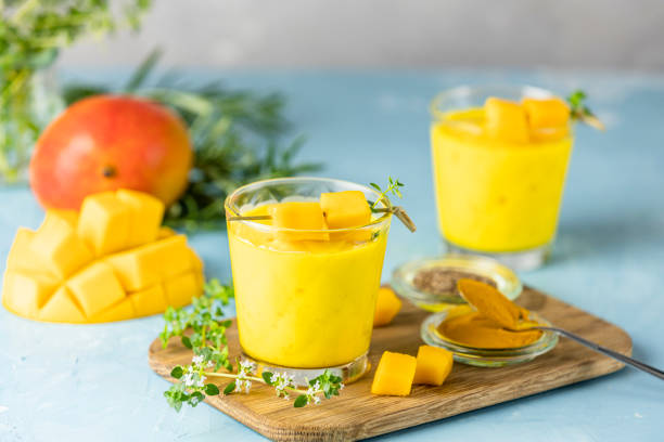 Yellow Indian mango yogurt drink Mango Lassi or smoothie with turmeric and saffron. Healthy probiotic Indian cold summer drink on blue background stock photo