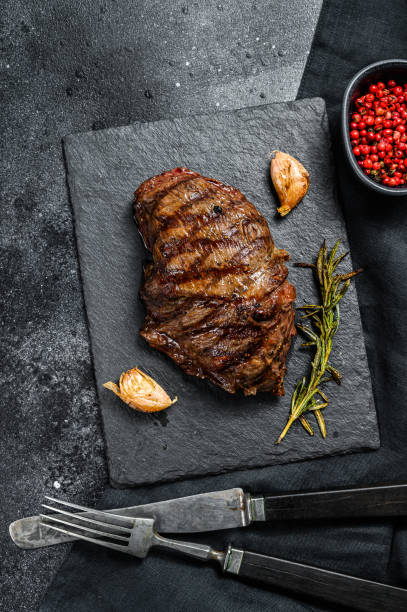 istock Grilled Top Blade steak on a stone Board, marbled beef. Black background. Top view 1249641612