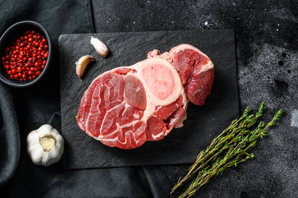 istock Raw beef ossobuco on a table with spices. Black background. Top view 1249643806