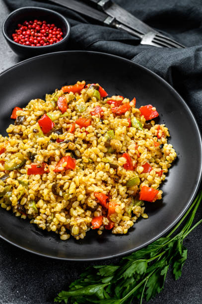 istock Bulgur with vegetables and meat on a plate. Black background. Top view 1249646226