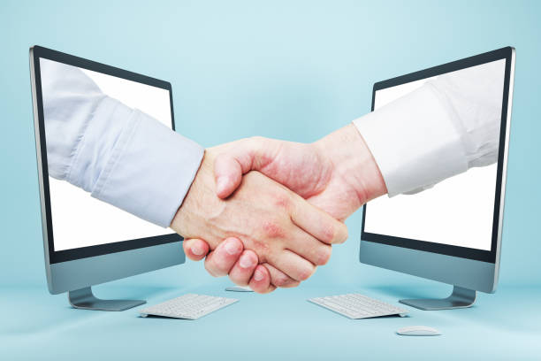 istock Businessmen shaking hands through computer screens on blue background 1249647322